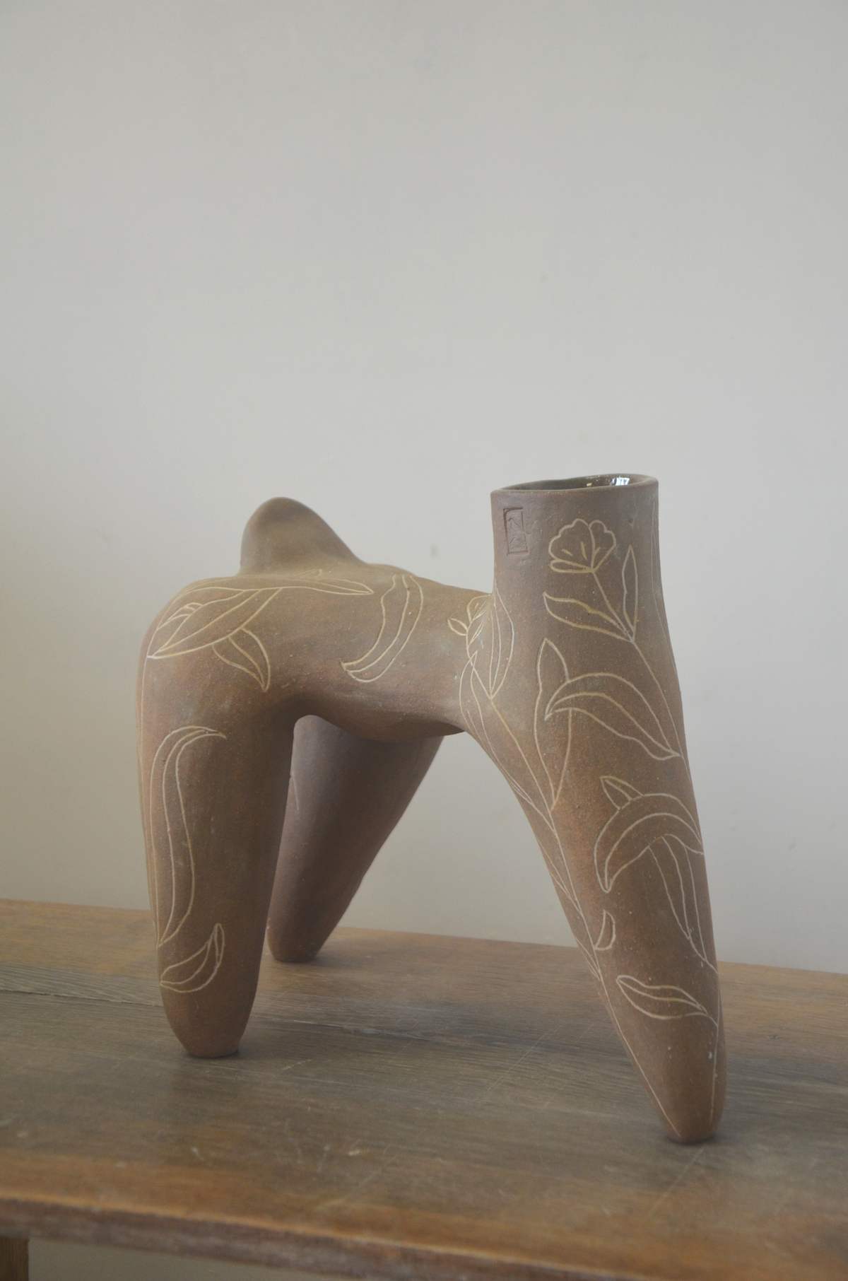 Pièce brune à quatre pieds ornée de feuillages blancs incisés, vue de trois quarts, ouverture au premier plan.