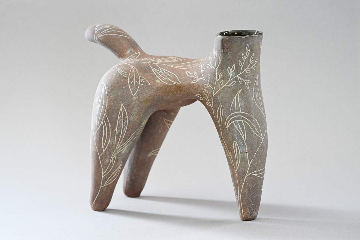 Pièce brune évoquant un animal à quatre pattes, ornée de feuillages blancs, sur fond gris.